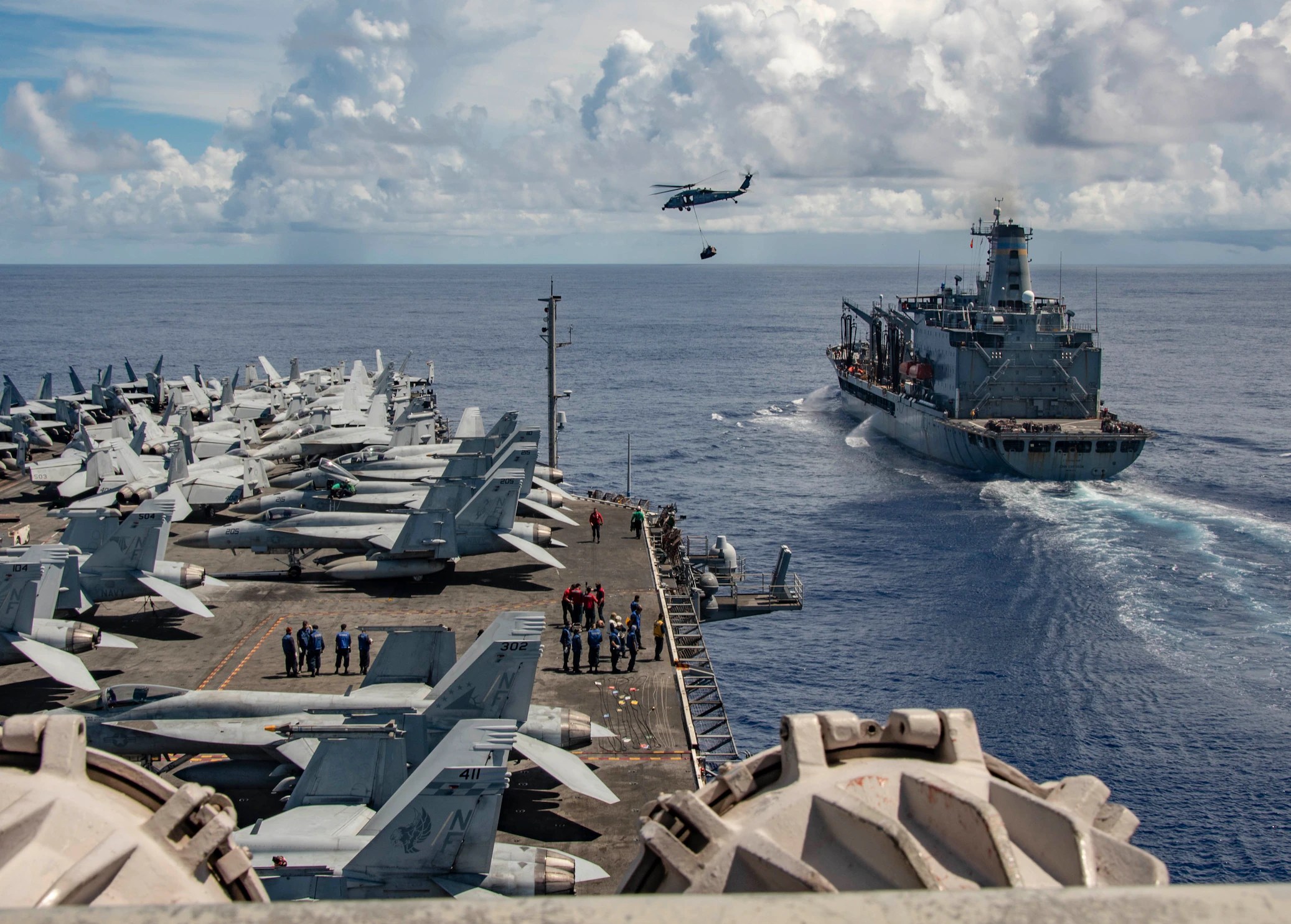 A US Navy Black Hawk helicopter carries a supply load from a fleet replenishment tanker to an aircraft carrier.